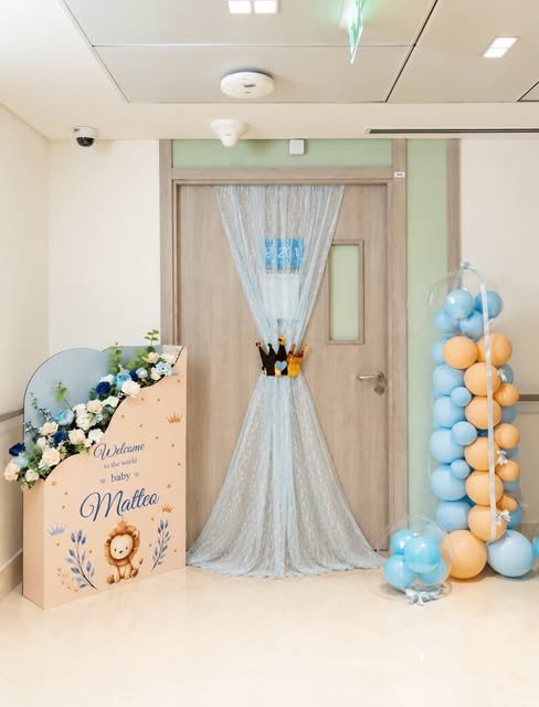 NILNA welcome baby setup in a hospital room with a floral welcome board and blue and gold balloons
